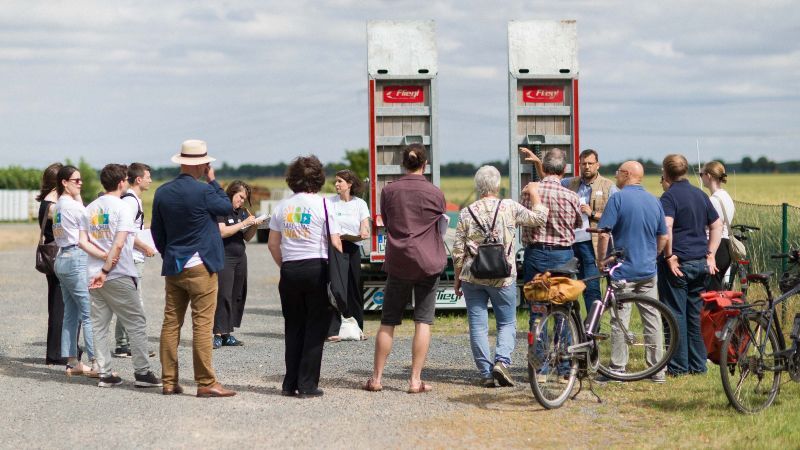 Teilnehmende einer Exkursion tauschen sich an einer Agri-PV-Anlage im Rheinischen Revier über die Verbindung von Landwirtschaft, Energieerzeugung und regionalem Strukturwandel aus. Die Anlage zeigt, wie Flächennutzung und erneuerbare Energien in der Bioökonomie zusammengedacht werden können.